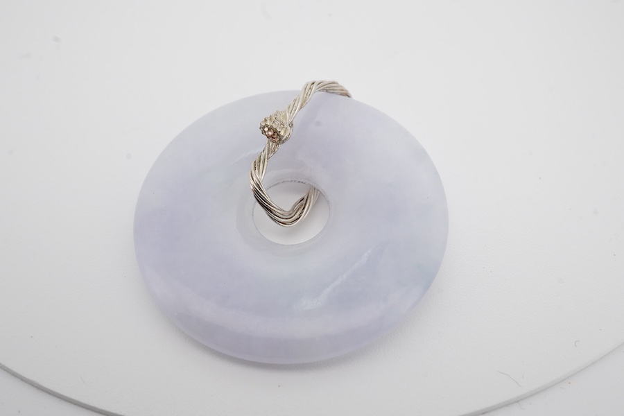 A jadeite pendant, designed as a disc of mottled white/pale lavender jadeite, to a bail of coiled wire, length 4.5cm, gross weight 12 grams, Condition: good